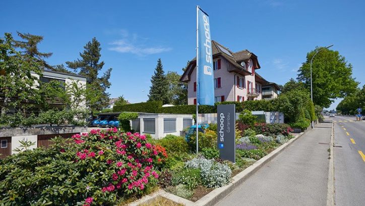 Eingang und Gartenanlage von Schoop Gartenbau mit Firmenschild und Fahne in Lenzburg, Karriere und Lehrstelle Aargau
